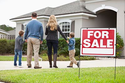 Family in front of home with for sale sign