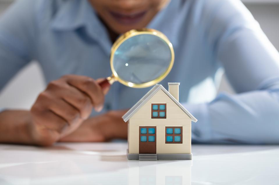 Man holding magnifying glass looking at miniature home