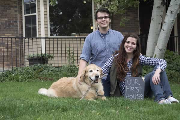 Couple sitting on grass in front of home with dog