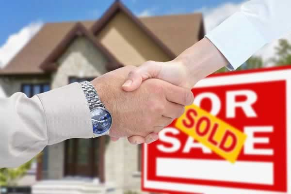 Hand shake in front of sold sign